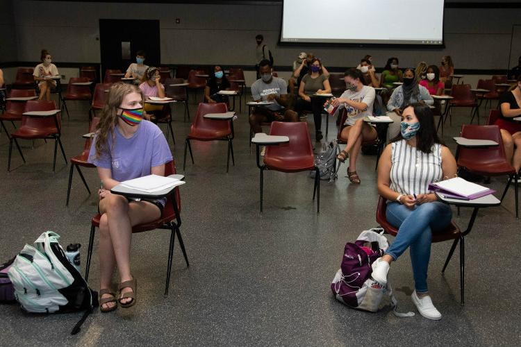 Masked students sit in a classroom with chairs spread out