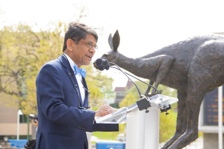阿格拉瓦尔总理对着麦克风讲话，背景是若隐若现的罗奥青铜雕塑