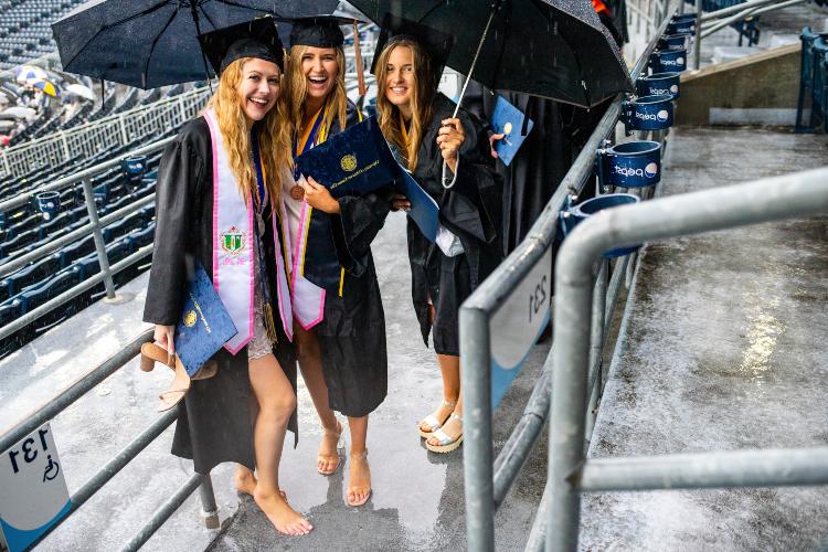 graduates smiling under an umbrella at The K