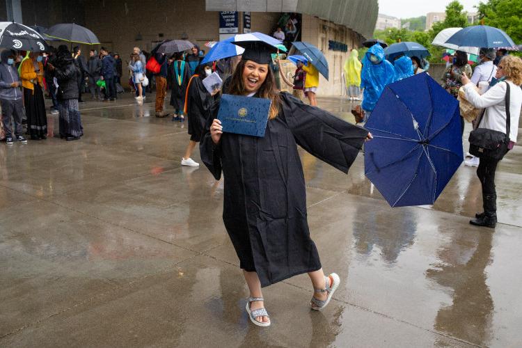 戴着徽章、拿着文凭、打着伞的女性在雨中