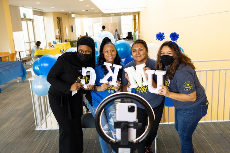 Four students take a selfie with a ring light, holding letters U-M-K-C.