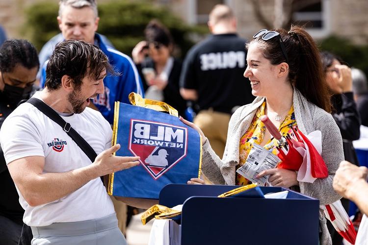 一名MLB代表将印有MLB品牌的手提袋和几袋薯片递给一个人. 两人都在微笑.