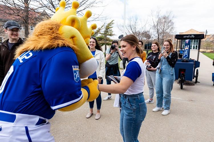 Sluggerrr holds a students hand; the student holds her arm out and laughs at Sluggerrr. 其他学生在后面笑着拍照.