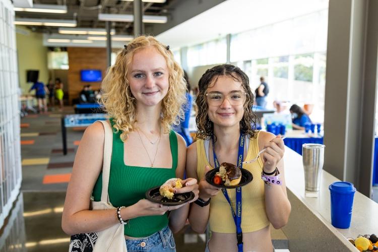 two students smile holding donuts