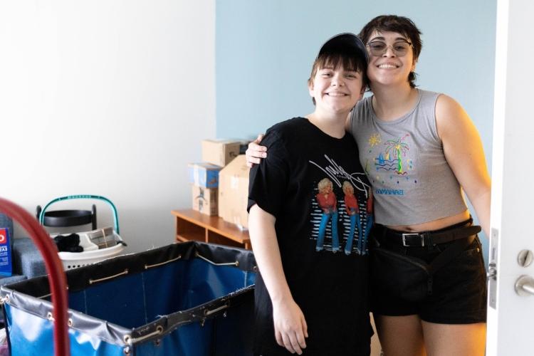 Roommates stand in their room smiling as they unpack at the Hospital Hill Apartments