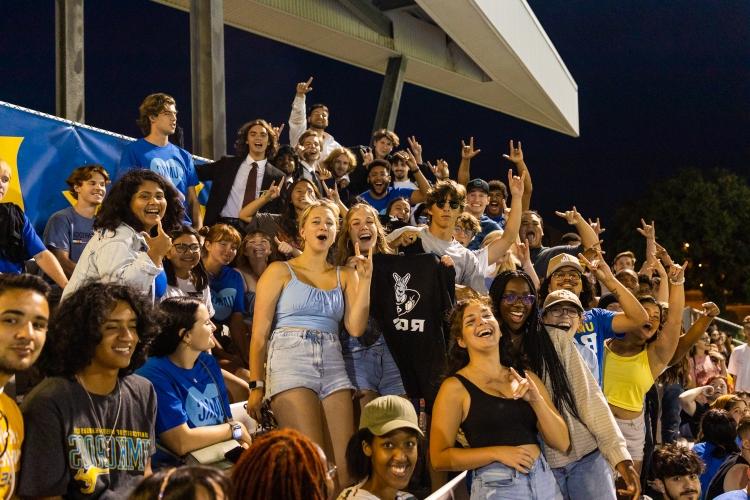 a group of fans smiles in the stands at the men's soccer game