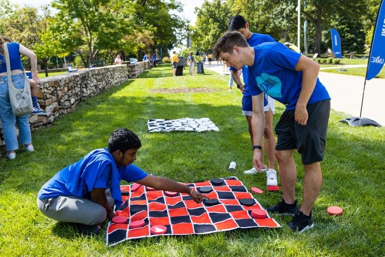 two people play checkers on a large checkers cloth outside