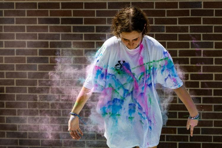 A student stands in a white shirt with color powder flying toward her, dying her shirt.