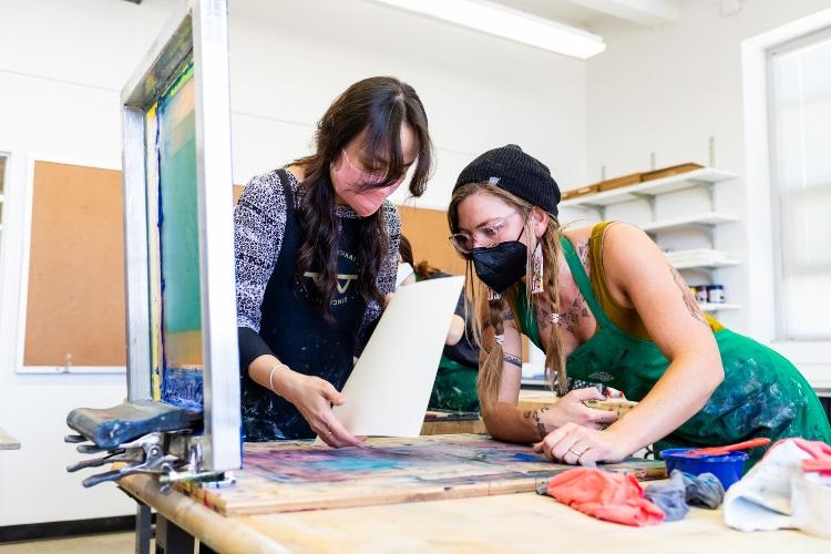 A professor helps a student with screen print in a studio