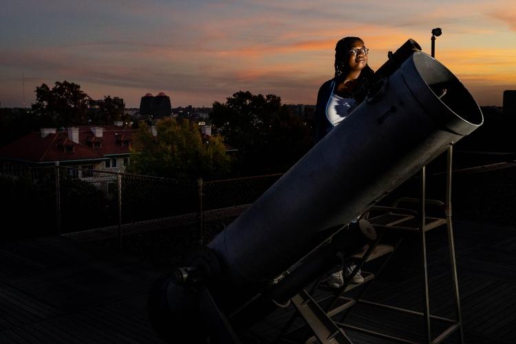 A student stands behind a large telescope at Wako Observatory at dusk