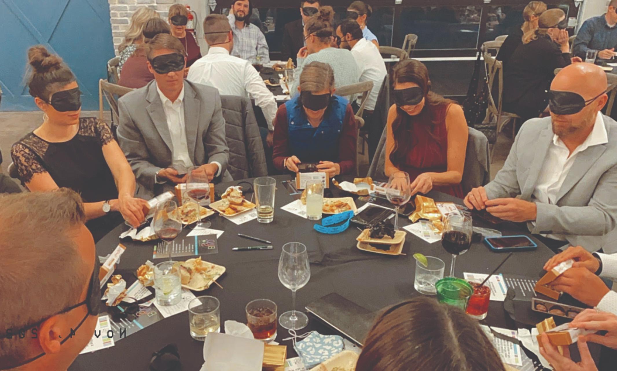 一群人蒙着眼睛坐在桌子旁吃饭 