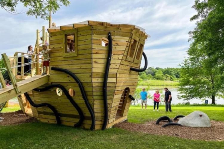 Children play in fort shaped like a pirate ship as parents watch in the background