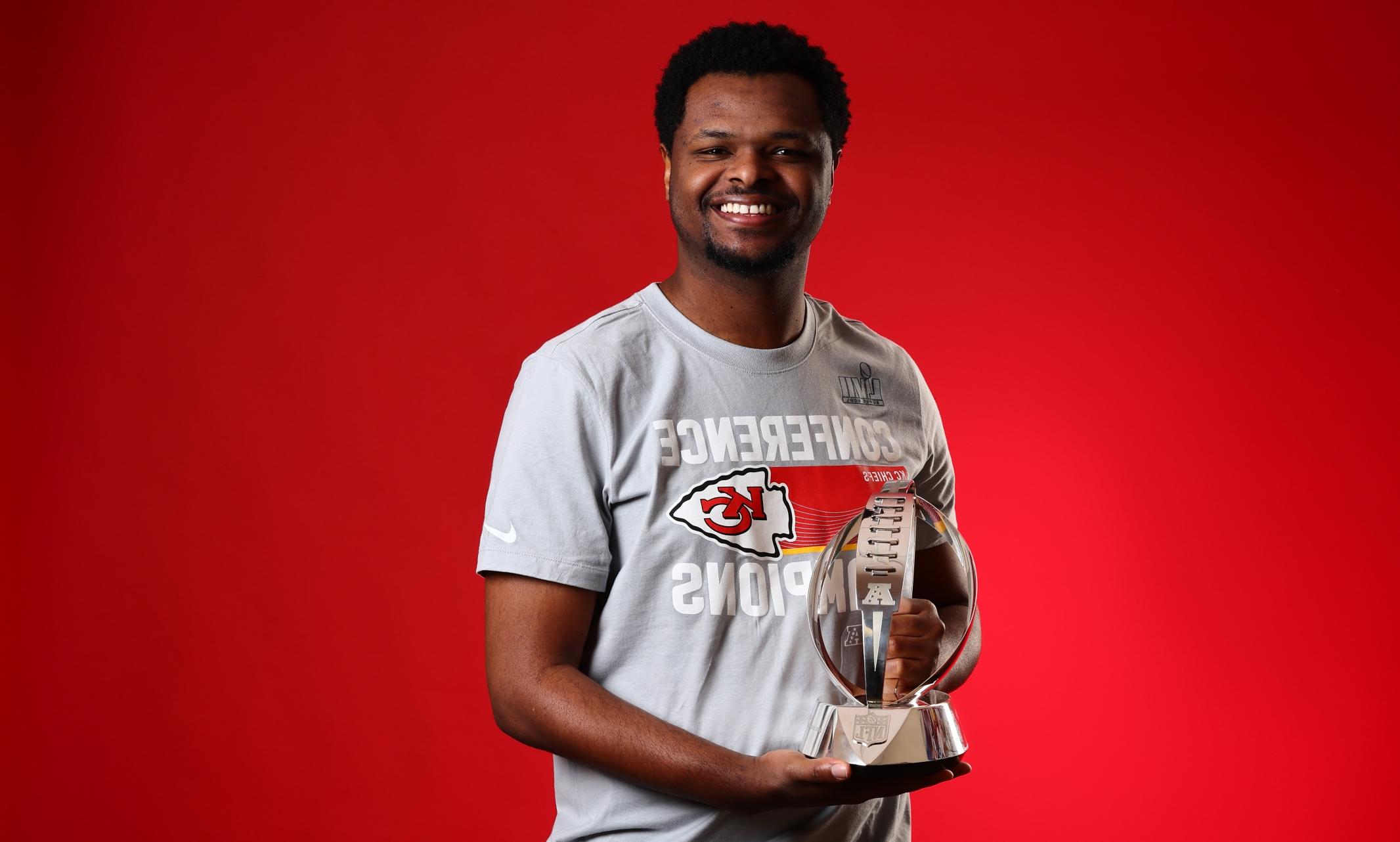 Ishmael Shumate holds the AFC Championship trophy smiling against a red backdrop