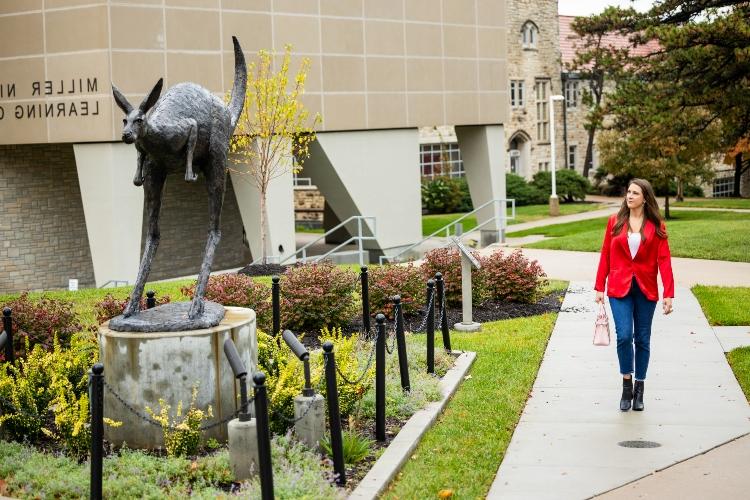 Meghan Jaben walks by the Corbin Roo statue on the UMKC Volker Campus wearing a bright red blazer