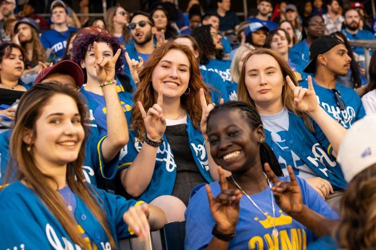UMKC students wearing UMKC and 皇室成员 jerseys, holdingtheir hands in a Roo Up gesture