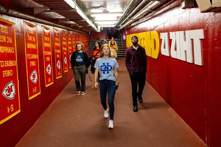 UMKC students at Arrowhead stadium walking through the chiefs branded tunnel that leads them straight on to the field that the chiefs play on